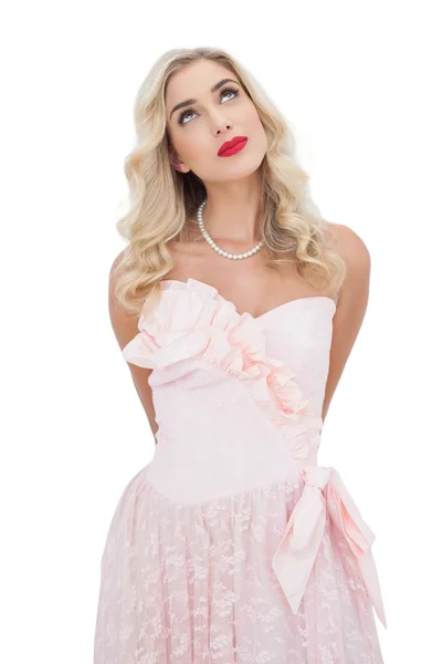 Мыслящая блондинка в розовом платье позирует, отводя взгляд — стоковое фото