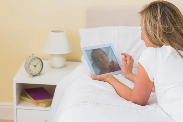 Mulher cuidadosa usando um tablet pc deitado em sua cama — Fotografia de Stock