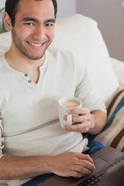 Sorrindo homem atraente beber café ao usar seu laptop — Fotografia de Stock