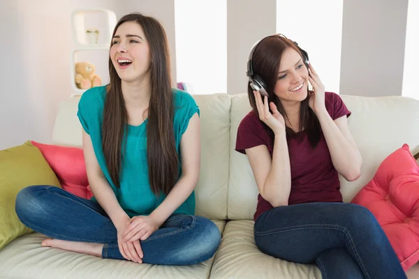 Chica escuchando música con su amigo a su lado en el sofá —  Fotos de Stock