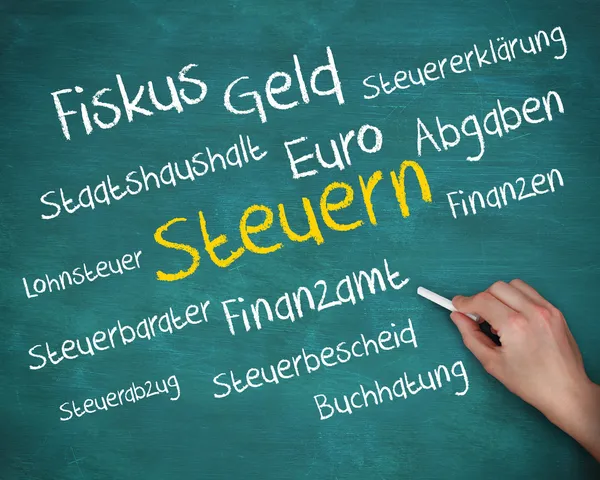Mão segurando um giz e escrevendo várias palavras sobre imposto em alemão — Fotografia de Stock