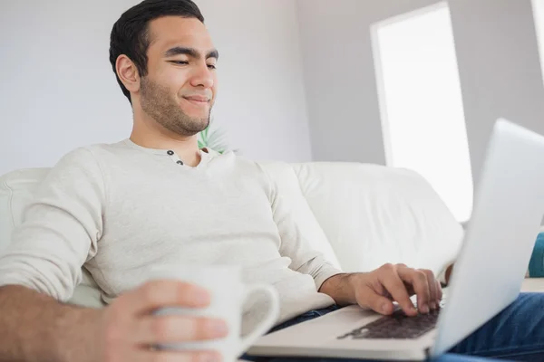 Vreedzame knappe man met koffie terwijl het gebruiken van zijn laptop — Stockfoto