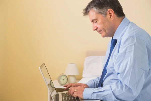 Homem focado usando um laptop sentado em uma cama — Fotografia de Stock