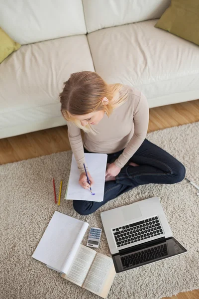 Blonde faisant ses devoirs et assise sur le sol en utilisant un ordinateur portable — Photo