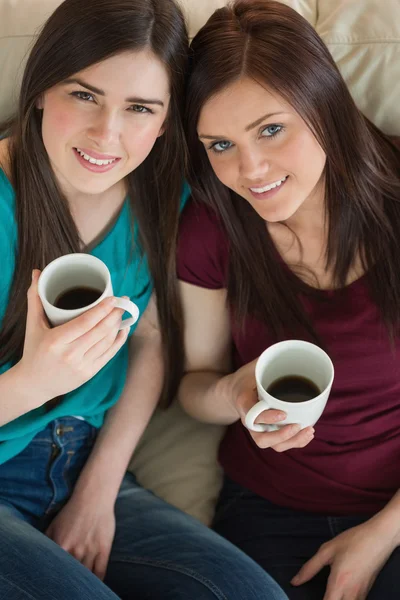 Kahve içer ve kanepede kameraya bakarak iki gülümseyen arkadaşlar — Stok fotoğraf