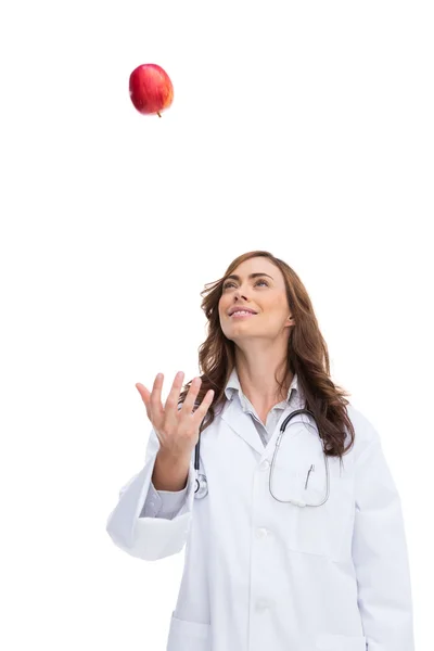 Smiling pretty doctor throwing apple — Stock Photo, Image