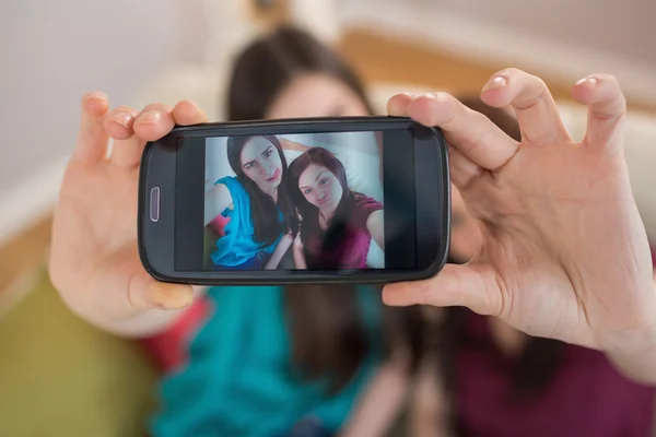 考虑与智能手机的 selfie 坐在沙发上的两个快乐朋友 — 图库照片