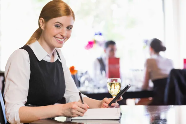 Lächelnde Geschäftsfrau mit Telefon und Schreiben, während sie in die Kamera schaut — Stockfoto