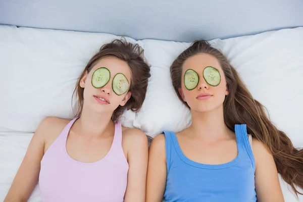 Amigos relaxando na cama com pepino nos olhos — Fotografia de Stock