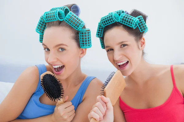 Friends in hair rollers singing into their hairbrushes — Stock Photo, Image
