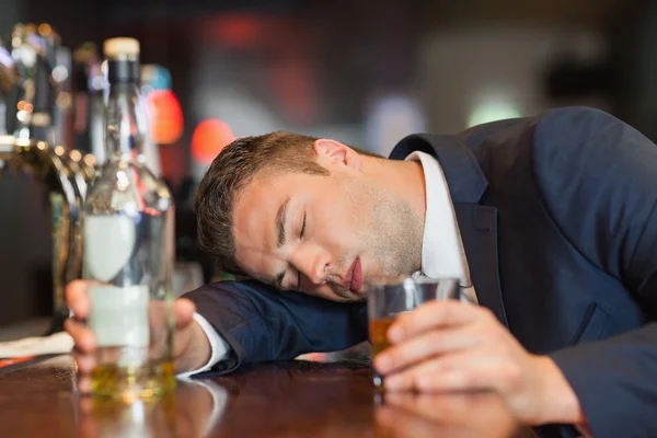 Unconscious businessman holding whiskey glass lying on a counter — Stock Photo, Image