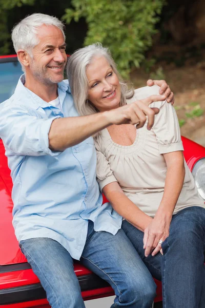 Sonriente pareja madura sentada en su convertible rojo — Foto de Stock