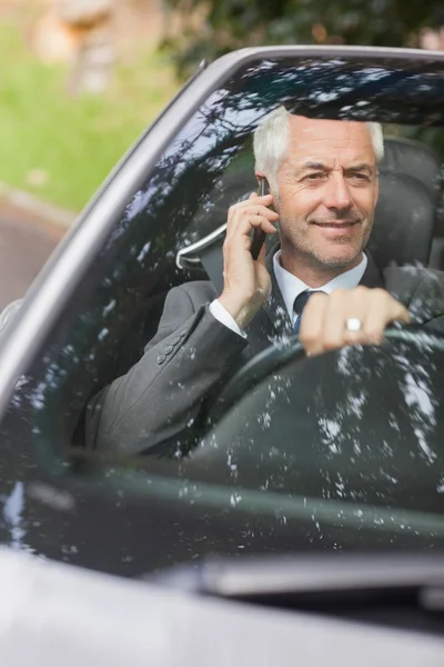 微笑驾驶昂贵的敞蓬车在电话上的商人 — 图库照片