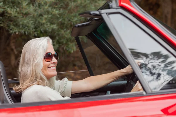 Счастливая зрелая женщина в солнечных очках водит красный кабриолет — стоковое фото