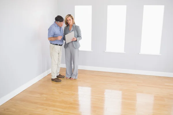 Serious blonde realtor showing a room and some documents to a potential buyer — Stock Photo, Image