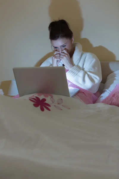 Pretty teen wearing bathrobe watching her laptop in the dark — Stock Photo, Image