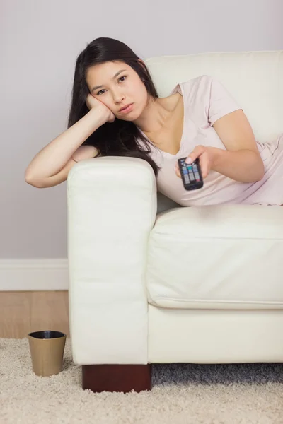 Bored asian girl lying on the sofa watching tv — Stock Photo, Image