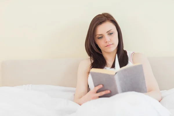 Menina concentrada lendo um livro deitado em uma cama — Fotografia de Stock