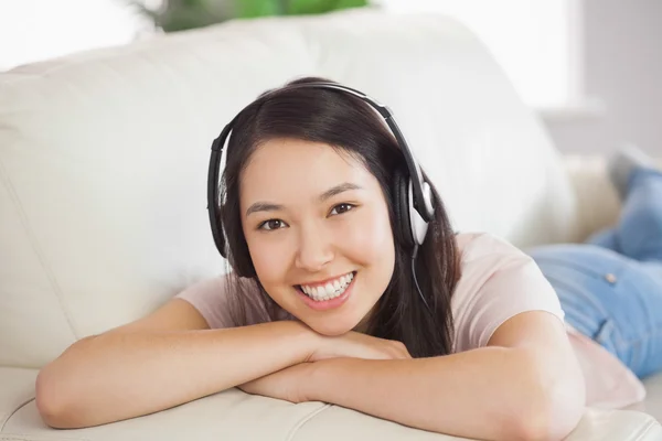 Sonriendo chica asiática acostada en el sofá y escuchando música —  Fotos de Stock