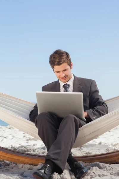 Hombre de negocios escribiendo en su computadora portátil en una hamaca y sonriendo — Foto de Stock