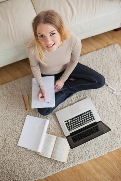 Gelukkige vrouw huiswerk doen en zittend op de vloer met behulp van laptop — Stockfoto