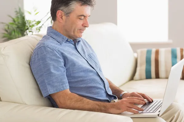 Pensando hombre sentado en el sofá usando el ordenador portátil — Foto de Stock