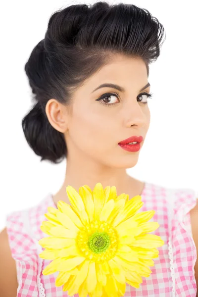Задумчивая модель черных волос, держащая цветок и смотрящая в камеру — стоковое фото