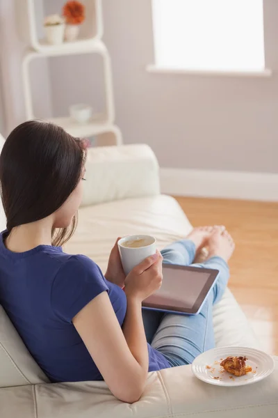 Молода жінка дивиться на планшетний ПК і тримає чашку кави — стокове фото