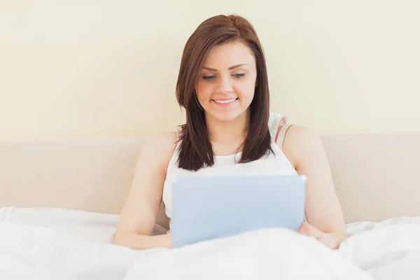 Lachende meisje met een tablet-pc liggend op een bed — Stockfoto