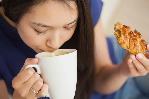 Mladá asijská žena popíjel kávu a drží pečivo — Stock fotografie
