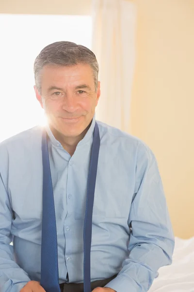 Uomo felice guardando la macchina fotografica seduta su un letto — Foto Stock