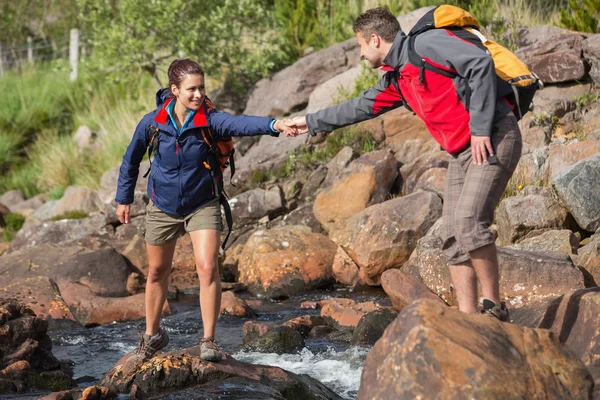 Man helping his smiling girlfriend to cross a river — Stock Photo, Image