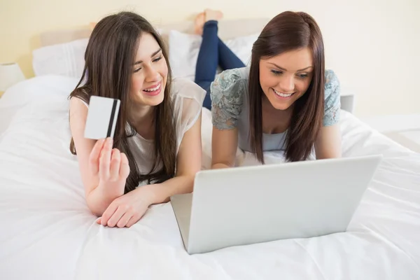Lächelnde Freunde kaufen mit Laptop im Bett online ein — Stockfoto