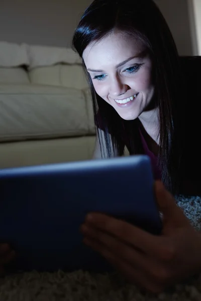 Leende brunett liggande på golvet med hjälp av TabletPC i mörkret — Stockfoto