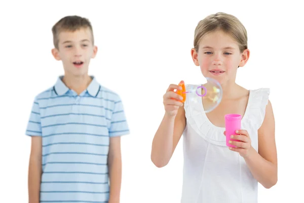 Девушка делает пузыри, пока ее брат смотрит на нее — стоковое фото