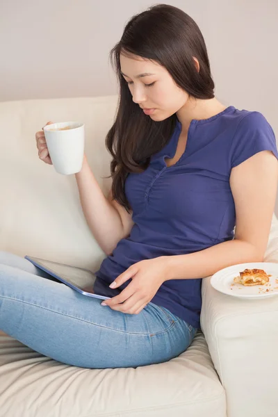 Jonge vrouw met behulp van haar tablet-pc en houden mok van koffie — Stockfoto