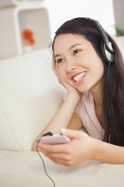 Gelukkig Aziatisch meisje liggend op de Bank en luisteren naar muziek met de smartphone — Stockfoto