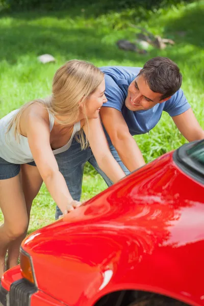 Happy couple pushing their broken down car Royalty Free Stock Images