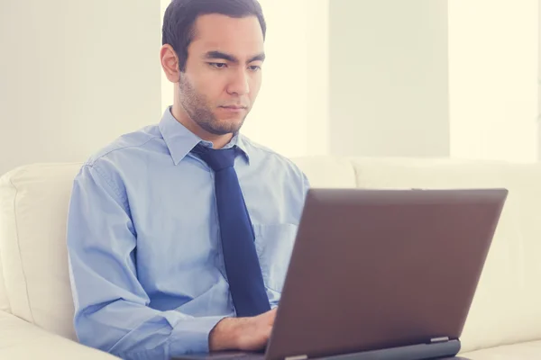 Stern man using a laptop sitting on a sofa — Stock Photo, Image