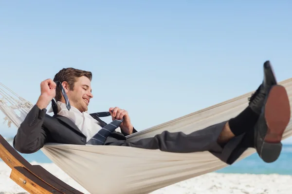 Smiling businessman lying in hamock taking off his tie — Stock Photo, Image