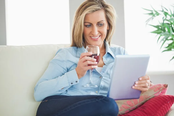 Sorrindo mulher bebendo vinho e usando um tablet pc — Fotografia de Stock