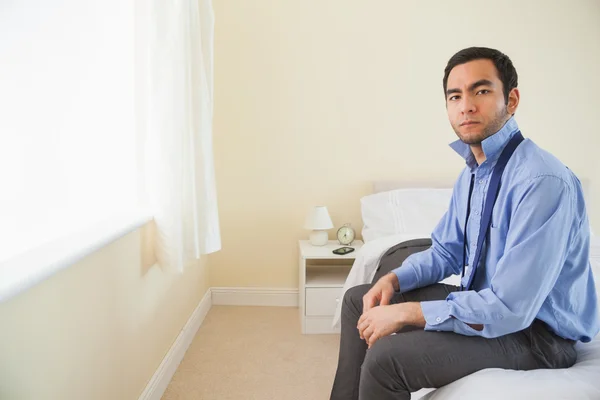 Stern homem olhando para a câmera e relaxante sentado em sua cama — Fotografia de Stock