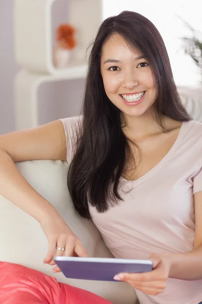 Bastante asiático chica usando su tableta en el sofá sonriendo a cámara — Foto de Stock