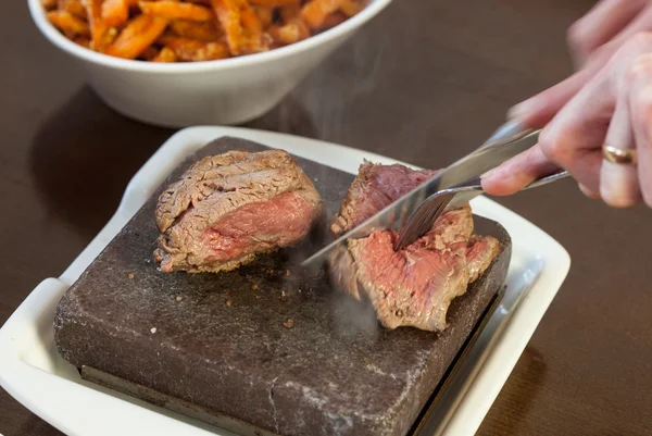 Steak sizzling on hot stone plate being sliced — Stock Photo, Image
