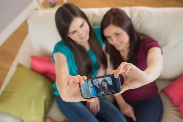 考虑与智能手机的 selfie 坐在沙发上的两个朋友 — 图库照片
