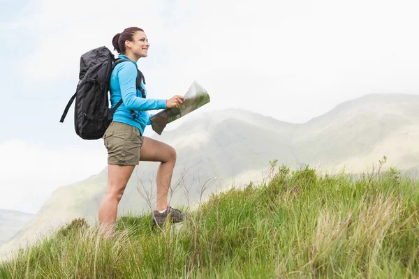 Caminhante atraente com mochila caminhando colina acima segurando um mapa — Fotografia de Stock