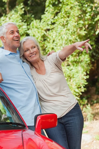 Mature couple leaning against their red cabriolet — Stock Photo, Image