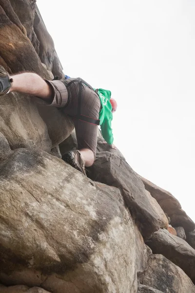 Determined man climbing a large rock face and seeing the summit — Stock Photo, Image