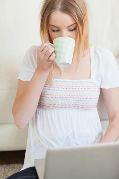 Женщина пьет кофе во время использования ноутбука — стоковое фото