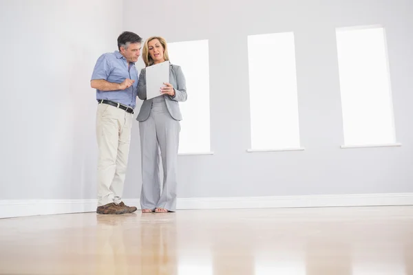 Konzentrierte blonde Maklerin zeigt einem potenziellen aufmerksamen Käufer ein Zimmer und einige Dokumente — Stockfoto